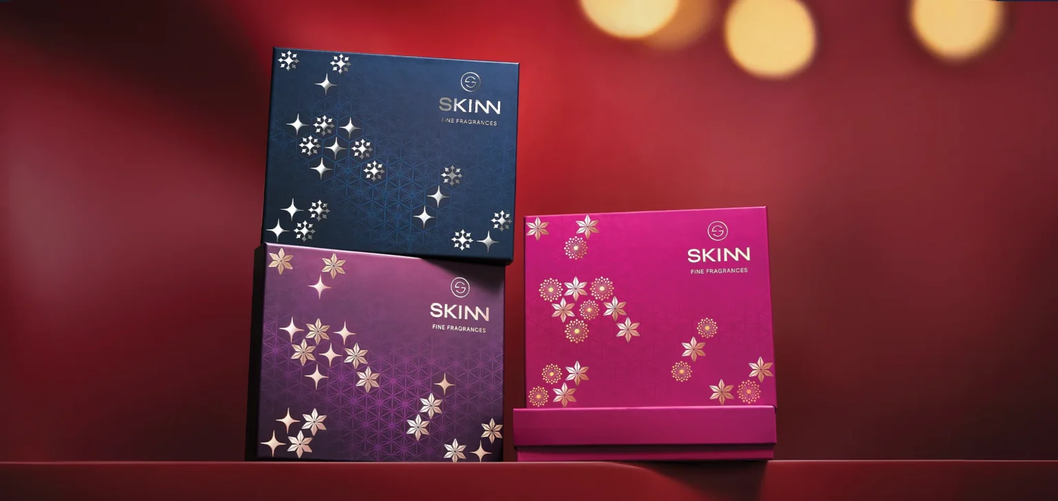 A collection of three elegantly stacked Titan Skinn festive gift boxes, showcasing the cohesive packaging design system created by Kern Culture. The display includes blue, magenta, and purple boxes with unique gold and silver foil motifs, representing the full range of men's and women's fragrance gift sets for the holiday season.